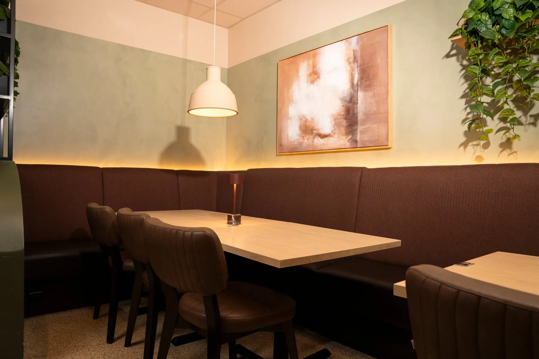 A corner table with a soft booth, low light and a painting on the wall.