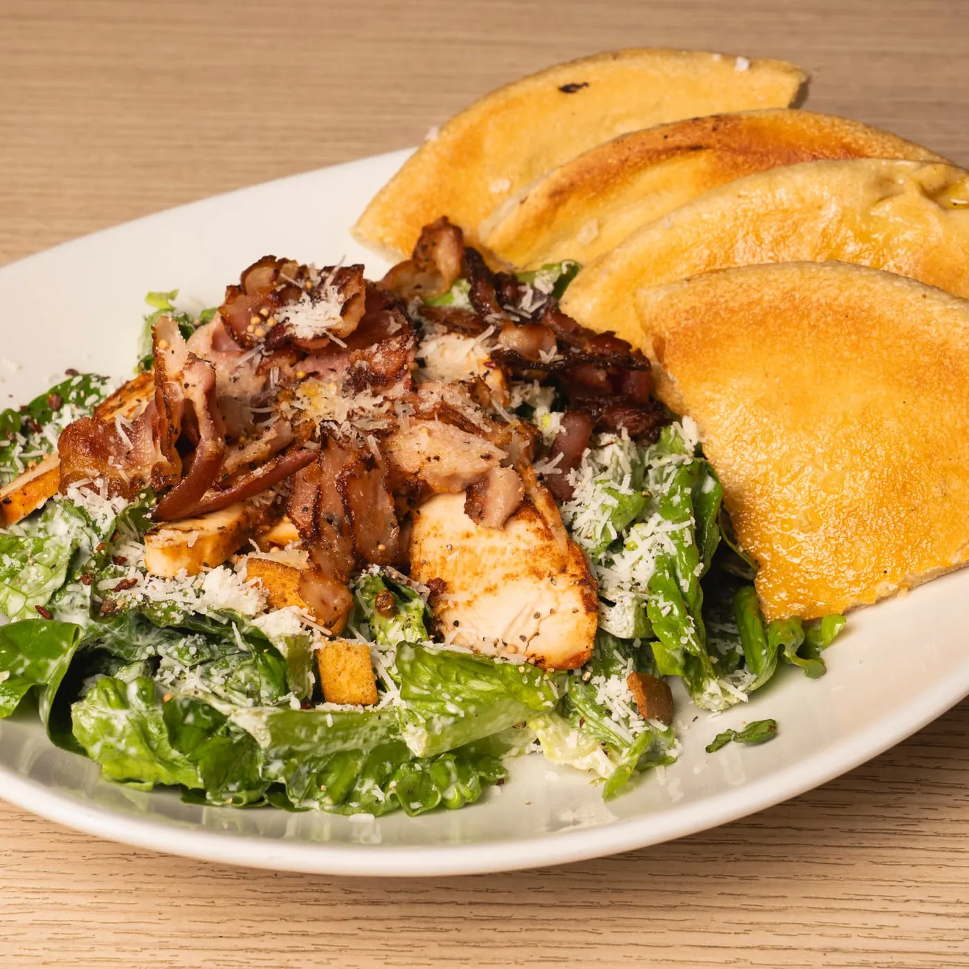 Caesar salad with chicken, bacon and bread on the side.