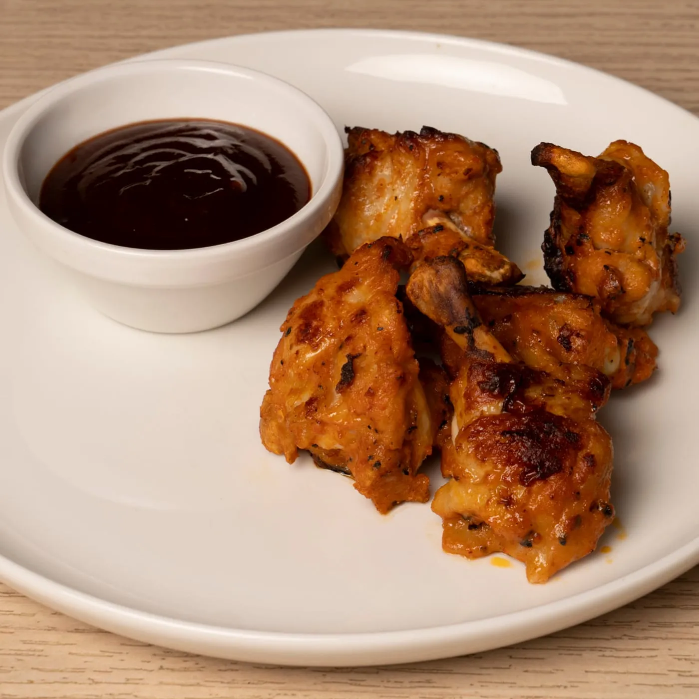 Five buffalo wings with a BBQ dip on a plate.